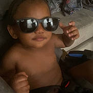 Million is registered to the contest to win money with this photo: child, indoor, sunglasses, braided_hair, couch, blanket, shirtless, cool, relaxed, person, young, seated, furniture, casual, home, portrait, smile, hand, dark, shadow