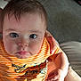 baby, child, infant, orange_striped_shirt, dinosaur_print, striped_pants, hand, person, face, eyes, hair, skin, sitting, indoor, carpet, couch, comfort, light, expression, pout