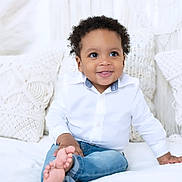 Lucas joined the competition — help win amazing prizes! toddler, child, smiling, white_shirt, blue_jeans, curly_hair, barefoot, bed, pillows, knitted_pillows, indoor, portrait, happy, cute, person, sitting, young_child, casual_clothing, cozy, bright