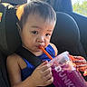 Kelly is registered to the contest to win money with this photo: toddler, child, car_seat, drink, straw, dunkin, purple_drink, blue_shirt, seatbelt, sunlight, window, car_interior, hand, face, expression, hair, beverage, summer, refreshment, casual