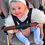 baby, child, stroller, headband, smiling, blue_eyes, white_clothing, socks, hand, seat, outdoor, sunlight, happy, face, person, infant, cute, warm_clothing, baby_carriage, closeup