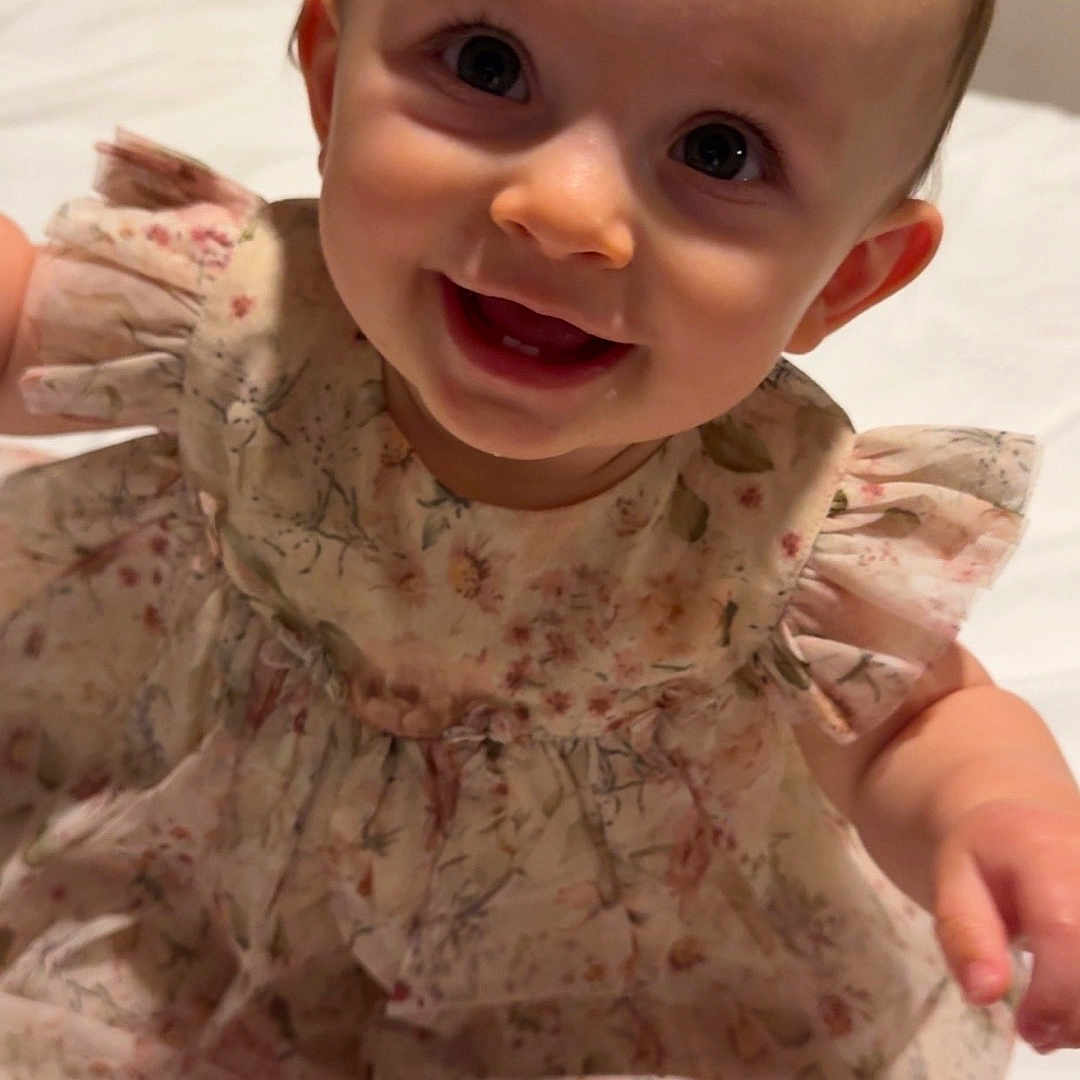 Eadie Rose is registered to the contest to win money with this photo: baby, bed, child, clothing, cute, dress, eyes, face, floral_pattern, hair, happy, indoors, infant, person, portrait, sitting, skin, smile, white_background, young