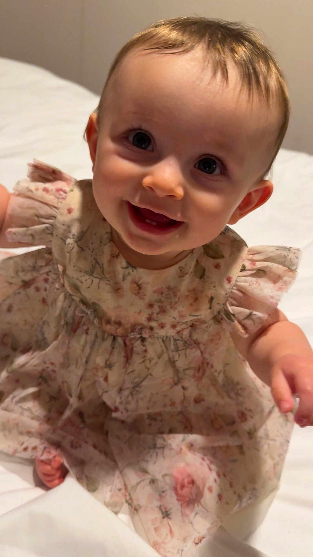 Eadie Rose is registered to the contest to win money with this photo: baby, child, smile, dress, floral_pattern, happy, face, eyes, cute, infant, person, sitting, skin, hair, indoors, bed, white_background, young, portrait, clothing