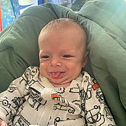 Kingston Ditoro is registered to the contest to win money with this photo: baby, infant, tongue_out, smiling, onesie, patterned_clothing, blanket, green_blanket, face, head, indoor, portrait, cute, playful, young_child, human, person, background_poster, tiger, animal_poster