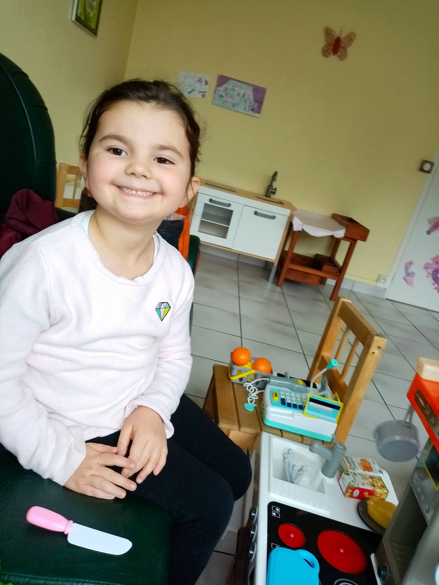Ilyana participe au concours pour gagner de l'argent avec cette photo : baby_toddler_clothing, chair, child, event, face, fun, happy, human_leg, joint, joy, knee, lap, person, picture_frame, play, room, smile, sock, standing, t_shirt