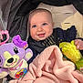 Ariya is registered to the contest to win money with this photo: baby, blanket, blue_eyes, child, clothing, cozy, cute, face, happy, indoor, infant, person, pink, plush_toy, portrait, purple, smiling, soft_toy, stroller, yellow