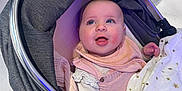 Ariya is registered to the contest to win money with this photo: baby, blanket, child, clothing, cozy, cute, eyelashes, fabric, face, hand, happy, head, indoors, infant, person, pink, smile, stroller, wheel, white