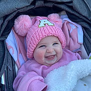 Ariya joined the competition — help win amazing prizes! apparel, baby, baby_clothes, blanket, child, clothing, cozy, cute, face, happy, headwear, infant, outdoor, pink_hat, pom_poms, portrait, smiling, snuggled, stroller, warm
