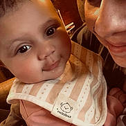 Aliyah is registered to the contest to win money with this photo: baby, adult, face, smile, bib, indoor, close_up, person, child, cute, warm_lighting, portrait, clothing, happy, skin, head, eyes, expression, holding, family