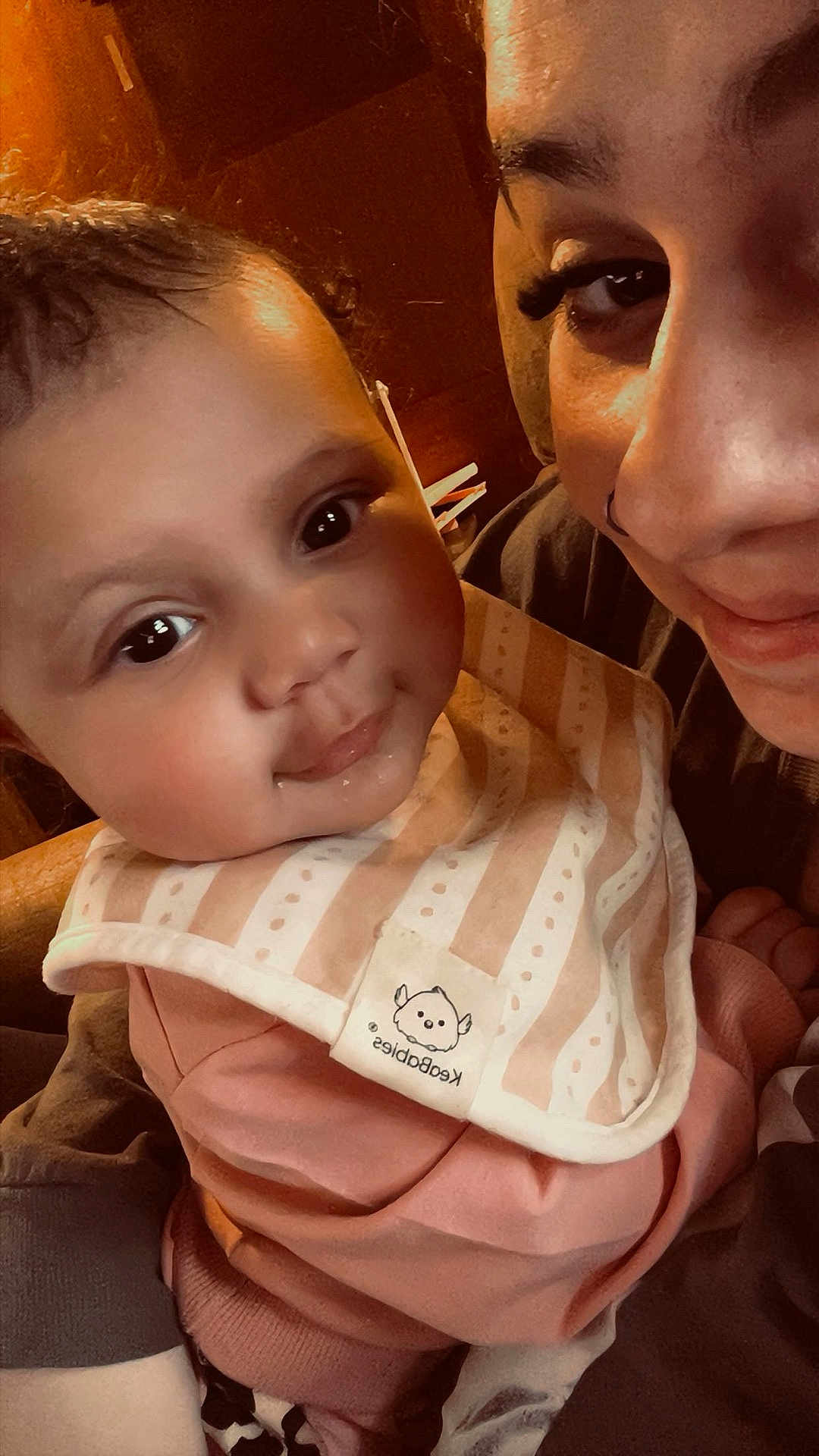 Aliyah is registered to the contest to win money with this photo: baby, adult, face, smile, bib, indoor, close_up, person, child, cute, warm_lighting, portrait, clothing, happy, skin, head, eyes, expression, holding, family