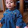 toddler, child, denim_dress, indoor, wooden_floor, table, chair, toy, pink_toy, curly_hair, face, big_eyes, sitting, person, blue_clothing, floor, furniture, closeup, casual, cute