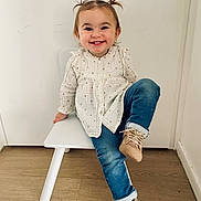 Elya a rejoint le concours — aidez-le/la à gagner de superbes lots ! child, toddler, smiling, sitting, white_chair, blue_jeans, beige_shoes, pigtails, long_sleeve_shirt, wooden_floor, indoor, white_wall, cute, happy, casual_clothing, playful, young_child, portrait, small_chair, buttoned_shirt
