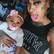 Natasha joined the competition — help win amazing prizes! baby, woman, tattoos, pacifier, headband, clothing, hand, face, person, indoor, expression, black_top, nail_polish, earrings, tongue_out, baby_clothes, portrait, holding, furniture, colorful