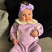 Monroe is registered to the contest to win money with this photo: baby, child, smiling, headband, bow, purple_outfit, sitting, couch, cushion, cozy, indoor, portrait, cute, happy, infant, clothing, hands, face, blue_eyes, soft_lighting