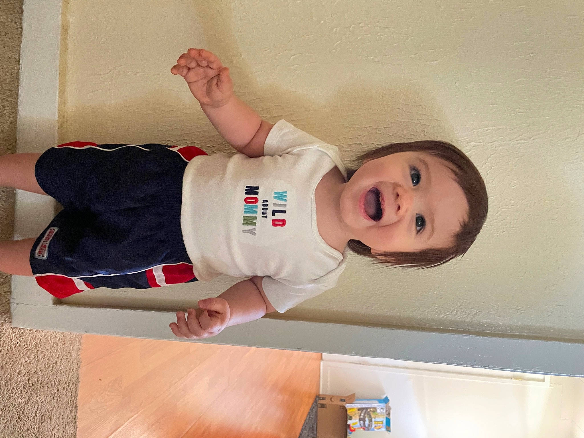 Uriah is registered to the contest to win money with this photo: arm, baby, baby_toddler_clothing, balance, child, elbow, finger, fun, happy, hardwood, hat, knee, person, room, sleeve, smile, standing, t_shirt, thigh, toddler