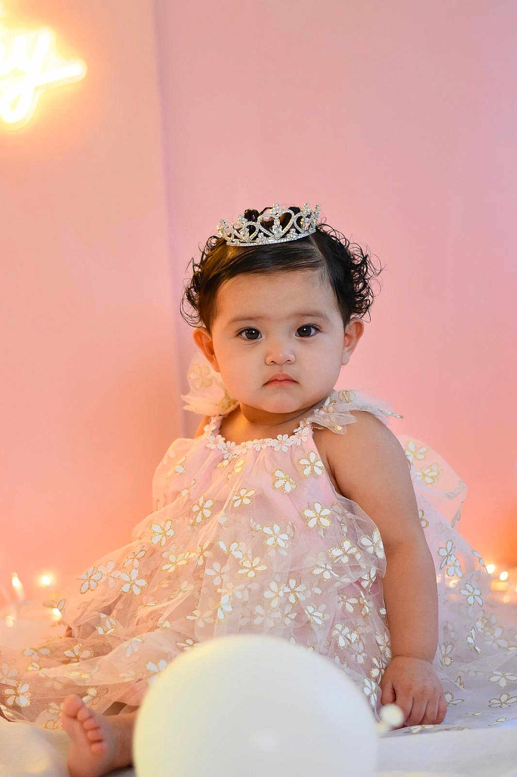 Madison joined the competition — help win amazing prizes! baby, child, tiara, dress, pink_background, balloon, flower_pattern, curly_hair, sitting, portrait, cute, indoors, soft_lighting, decorative_lights, serious_expression, young_child, celebration, birthday, adorable, fashion