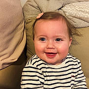 Giulia participe au concours pour gagner de l'argent avec cette photo : baby, child, smiling, striped_shirt, hair_clip, indoor, couch, blanket, happy, portrait, face, toddler, cozy, light_skin, blue_eyes, seated, clothing, cute, infant, home