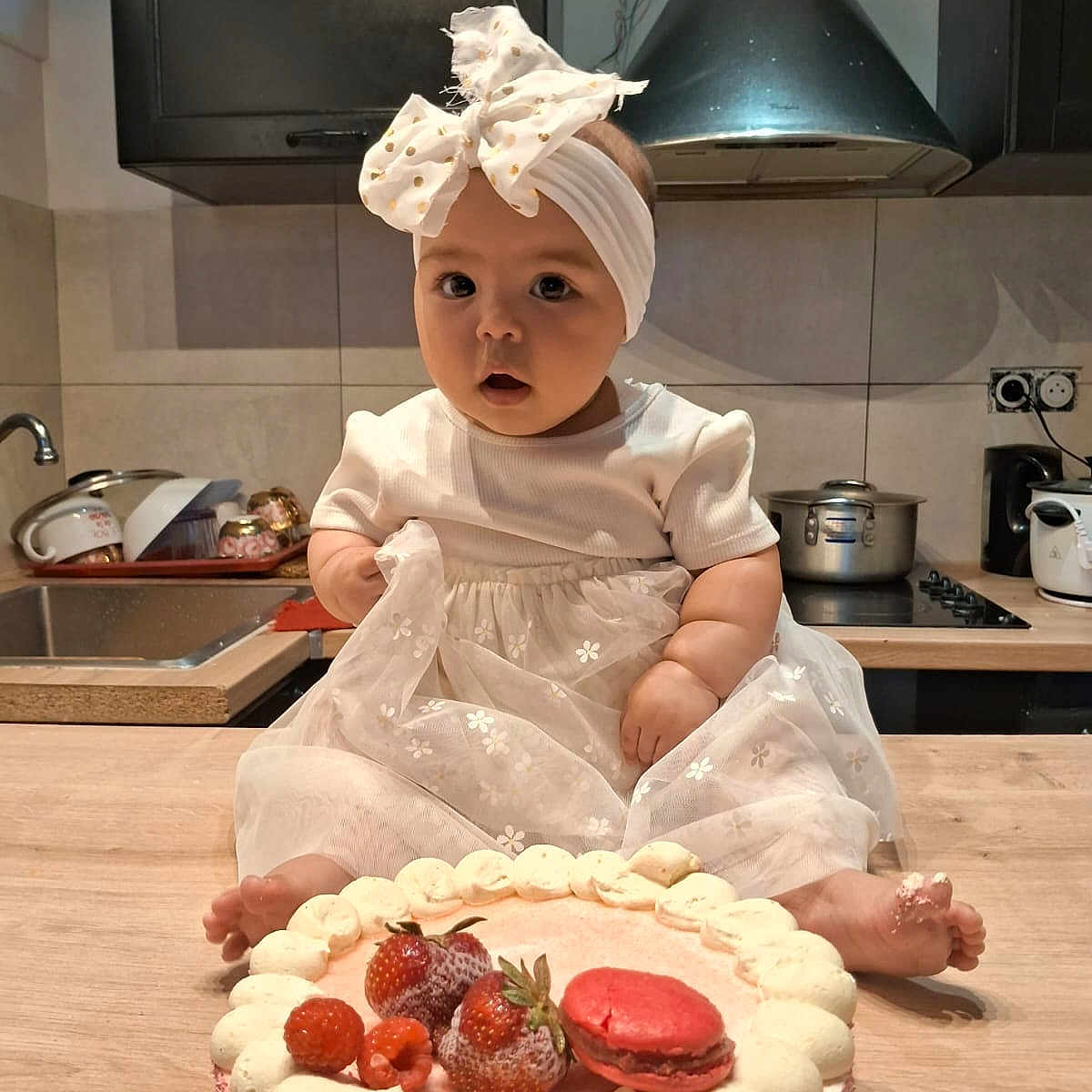 Christelle participe au concours pour gagner de l'argent avec cette photo : appliance, baby, cake, child, cooking, countertop, cute, dessert, food, foot, frosting, headband, indoor, kitchen, macaron, portrait, pots, sink, strawberries, white_dress