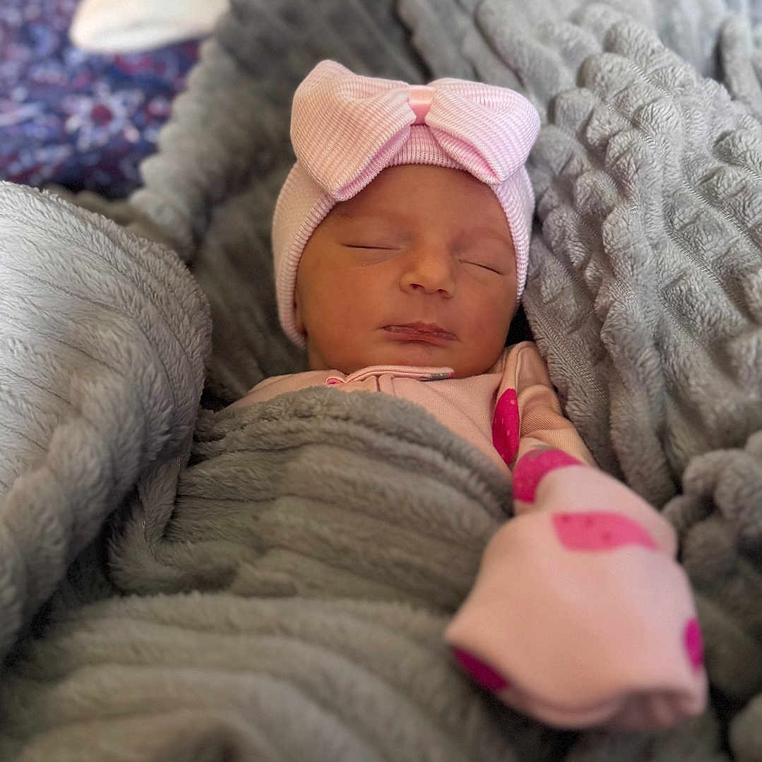 Kaylene is registered to the contest to win money with this photo: baby, bed, blanket, bokeh, bow, cozy, cute, face, head, indoor, nap, newborn, nursery, pajamas, peaceful, pink_hat, portrait, sleeping, soft_texture, swaddle