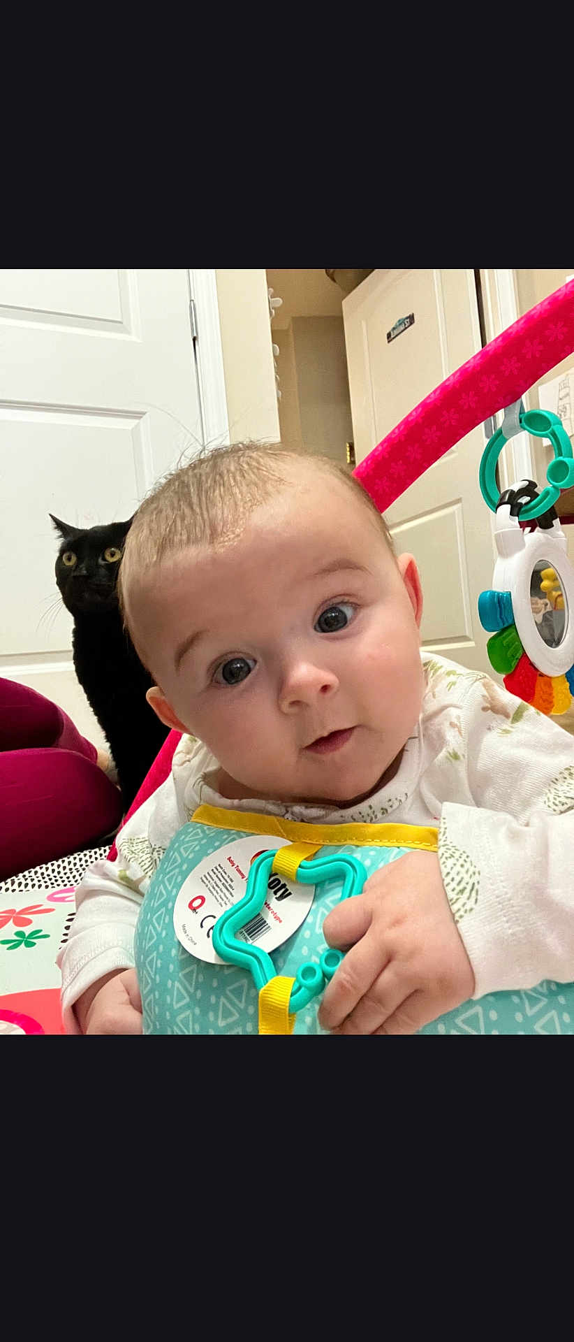 Angelina joined the competition — help win amazing prizes! baby, infant, cat, black_cat, pet, surprised_face, toy, playmat, door, indoor, portrait, closeup, big_eyes, hands, clothing, nursery, floor, colorful, mirror_toy, photobomb