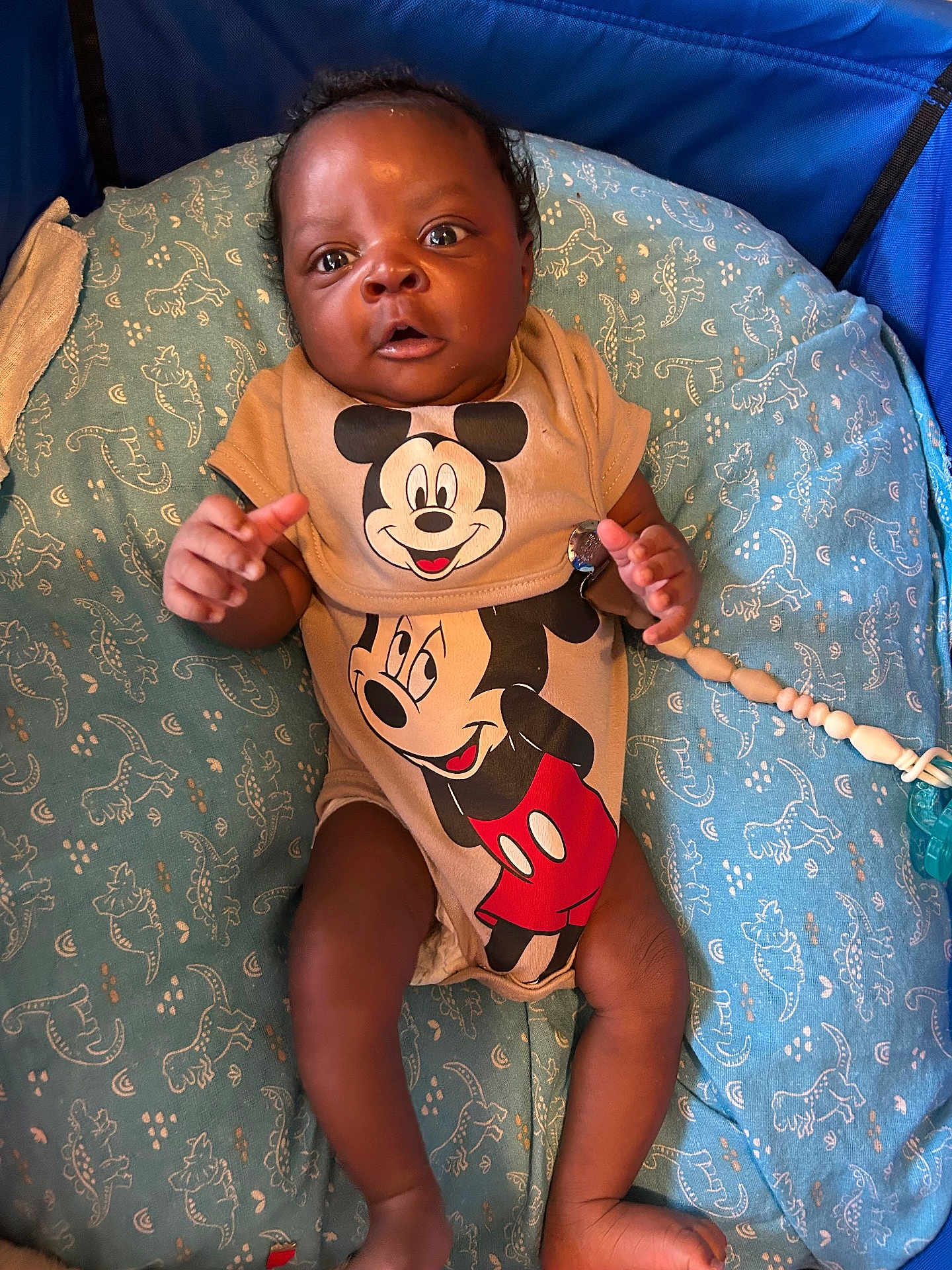Kyzan joined the competition — help win amazing prizes! baby, infant, mickey_mouse, onesie, blue_cushion, pattern, cute, child, lying_down, indoor, clothing, hand, foot, expression, face, person, comfort, toy_clip, fabric, closeup
