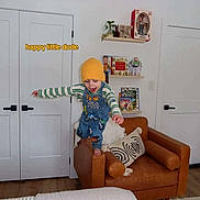 Kane joined the competition — help win amazing prizes! child, toddler, smiling, happy, standing, balancing, armchair, beanie, overalls, striped_shirt, indoor, living_room, furniture, cushion, bookshelf, toys, action_figure, decor, wooden_floor, text_overlay