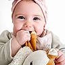 adorable, baby, chewing, child, closeup, clothing, cute, face, hand, happy, headband, indoors, infant, pink, plush_toy, portrait, smiling, soft_toy, white_background, young