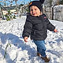 black_jacket, blue_jeans, brown_boots, child, cold_weather, daylight, fence, footprints, happy, hat, nature, outdoor, playful, snow, snowy_ground, sunny, toddler, trees, winter_clothing, young_kid