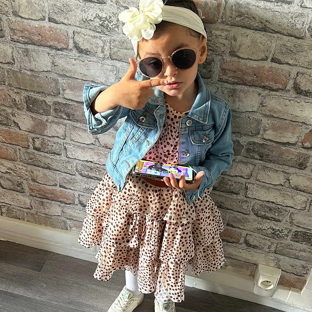 Jennah a rejoint le concours — aidez-le/la à gagner de superbes lots ! accessories, brick, cap, child, clothing, coat, face, female, footwear, girl, glasses, hat, head, pants, person, photography, portrait, shoe, sitting, sunglasses
