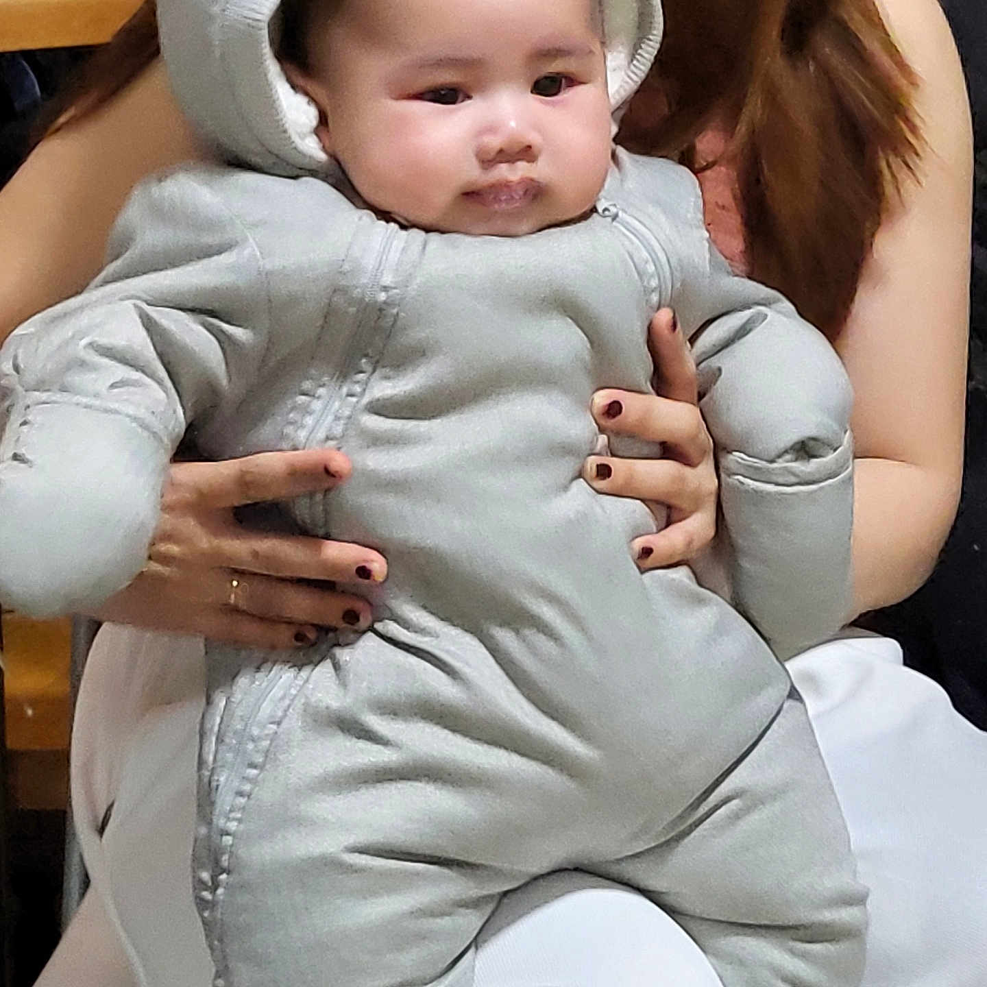 Kalel a rejoint le concours — aidez-le/la à gagner de superbes lots ! adult_hands, baby, chair, child, cozy, cute, expression, face, grey_clothing, holding, hood, indoor, nail_polish, padded_suit, person, portrait, seated, snowsuit, warm_clothing, white_pants