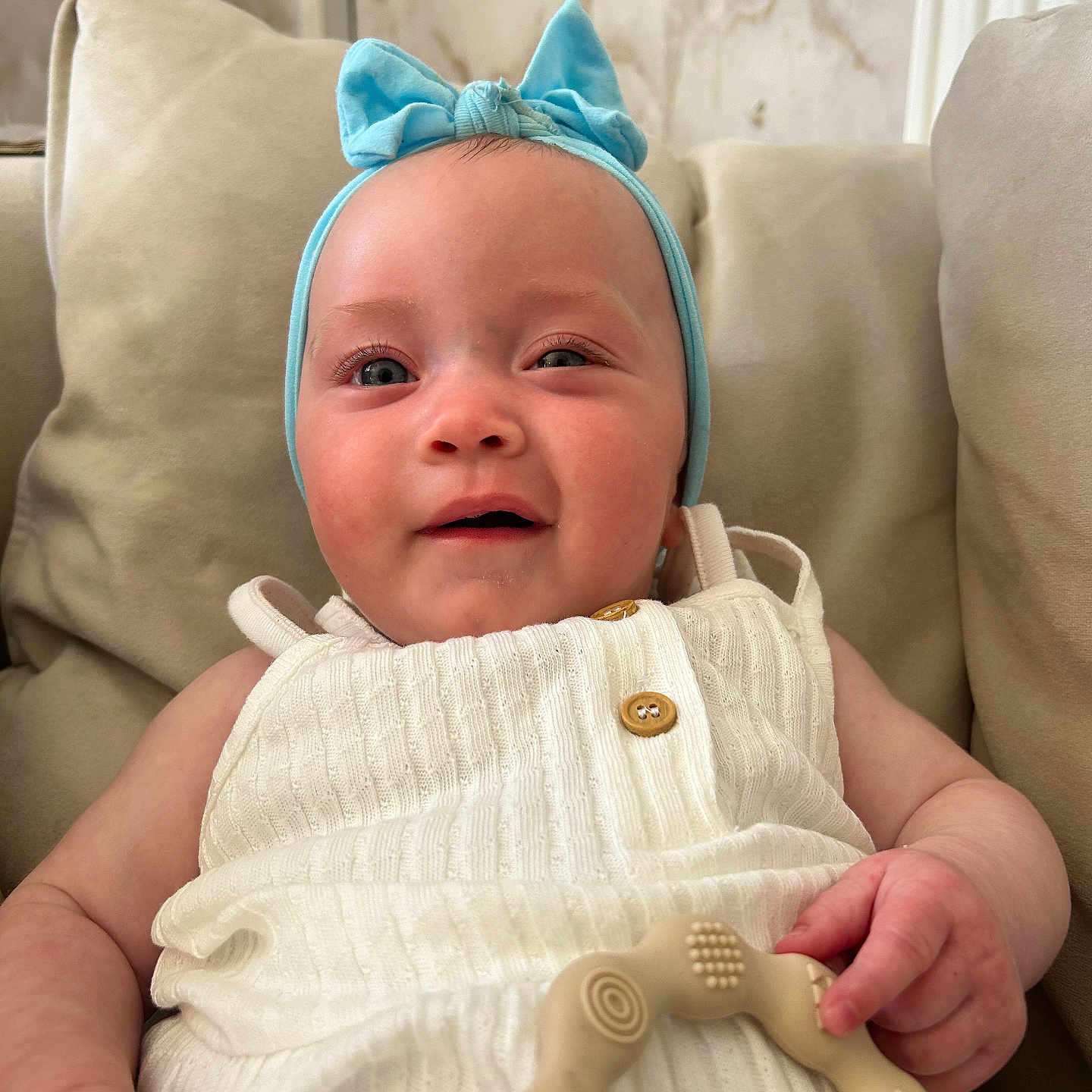 Lyra joined the competition — help win amazing prizes! baby, beige_cushions, blue_headband, button, child, closeup, couch, cute, face, hand, happy, headwear, indoor, infant, portrait, skin, smiling, teething_ring, texture, white_outfit