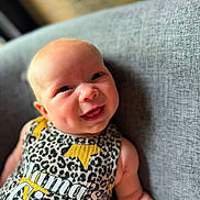 Averi is registered to the contest to win money with this photo: baby, smiling, infant, couch, clothing, leopard_print, text, mamas_girl, happy, portrait, face, cheeks, arm, indoor, child, cute, young, person, sitting, cozy