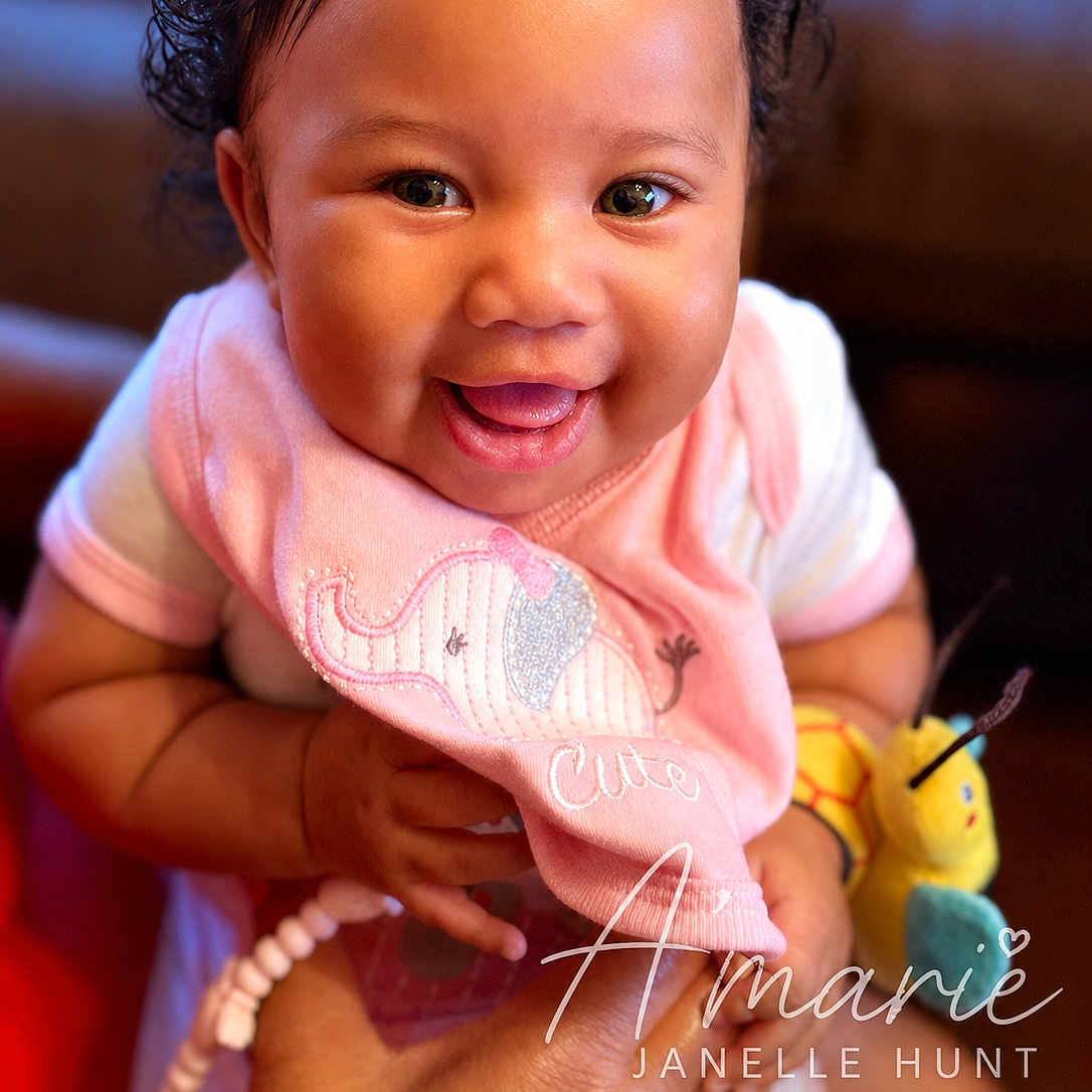Amarie joined the competition — help win amazing prizes! baby, smiling, pink_bib, elephant_embroidery, toy, hand, happy, closeup, infant, cute, child, person, portrait, indoors, warm_lighting, cheerful, holding, clothing, cute_expression, adorable