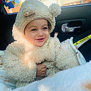 Ekam is registered to the contest to win money with this photo: baby, child, smiling, cute, fluffy_clothing, bear_costume, car_seat, blanket, toy, window, sunlight, face, hand, indoor, seatbelt, vehicle_interior, happy, infant, warm_clothing, portrait