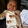 baby, child, smiling, tongue_out, onesie, lion_pattern, blanket, leather, black_leather, infant, cute, happy, cozy, young_child, face, person, clothing, lying_down, indoors, playful