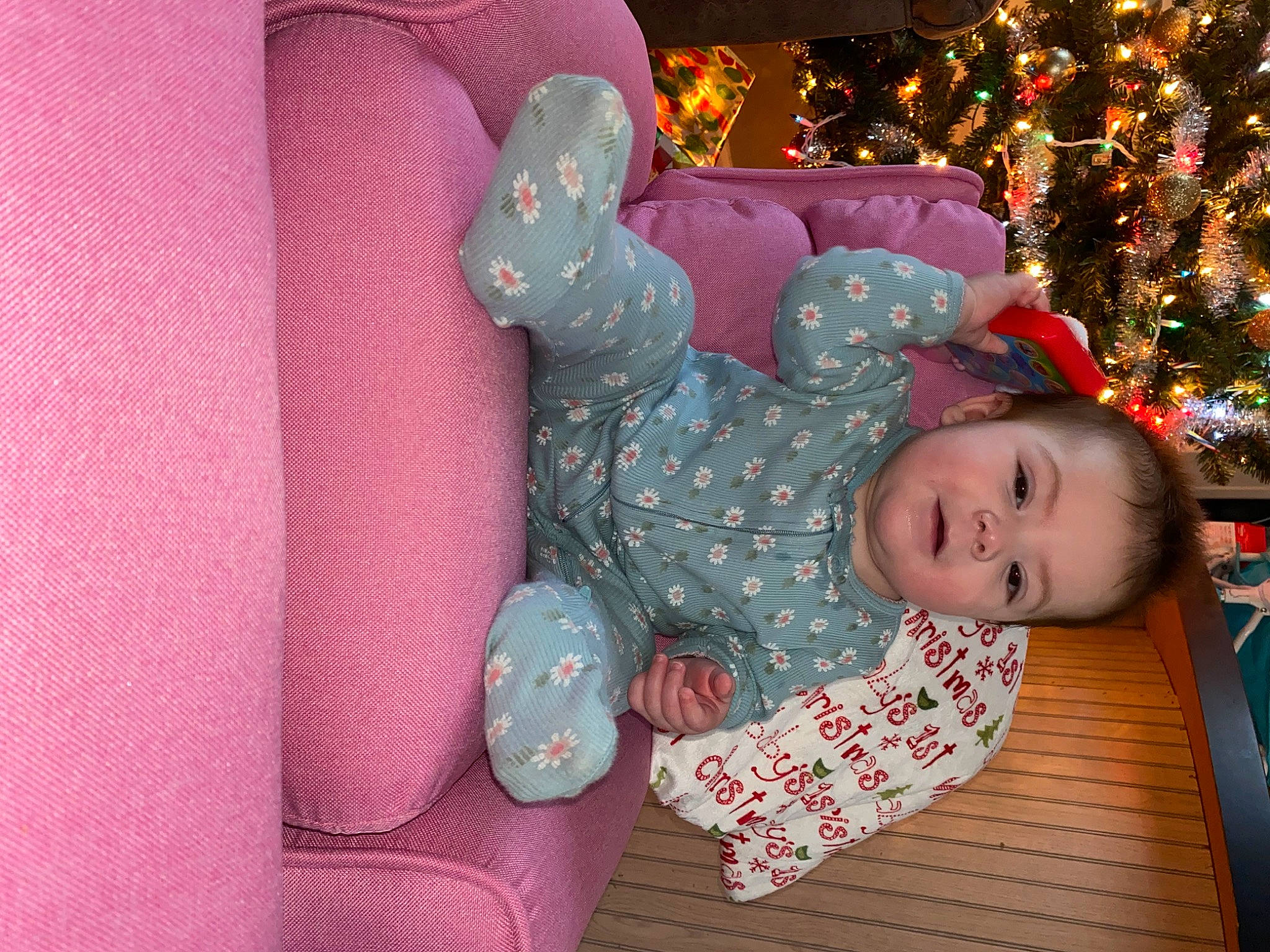 Ariella is registered to the contest to win money with this photo: baby, baby_toddler_clothing, child, christmas, christmas_decoration, christmas_ornament, christmas_tree, comfort, event, happy, head, holiday, linens, magenta, ornament, pattern, person, pink, room, sitting