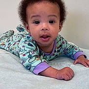 Kaylani joined the competition — help win amazing prizes! baby, bed, blanket, child, curly_hair, eyes, face, hand, indoors, infant, lock_screen, lying_down, pajamas, phone_screen, portrait, skin, technology, time_display, tummy, wall