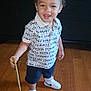 Kingstyn is registered to the contest to win money with this photo: toddler, child, smiling, standing, wooden_floor, tommy_hilfiger, shirt, shorts, white_sneakers, nike, black_dresser, drawer, striped_bag, baby_items, stick, curly_hair, indoor, happy, person, footwear