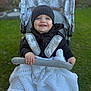 Myles is registered to the contest to win money with this photo: baby, child, smiling, stroller, blanket, knit, hat, beanie, outdoor, grass, happy, person, portrait, young_child, cute, clothing, seatbelt, hands, face, hoodie