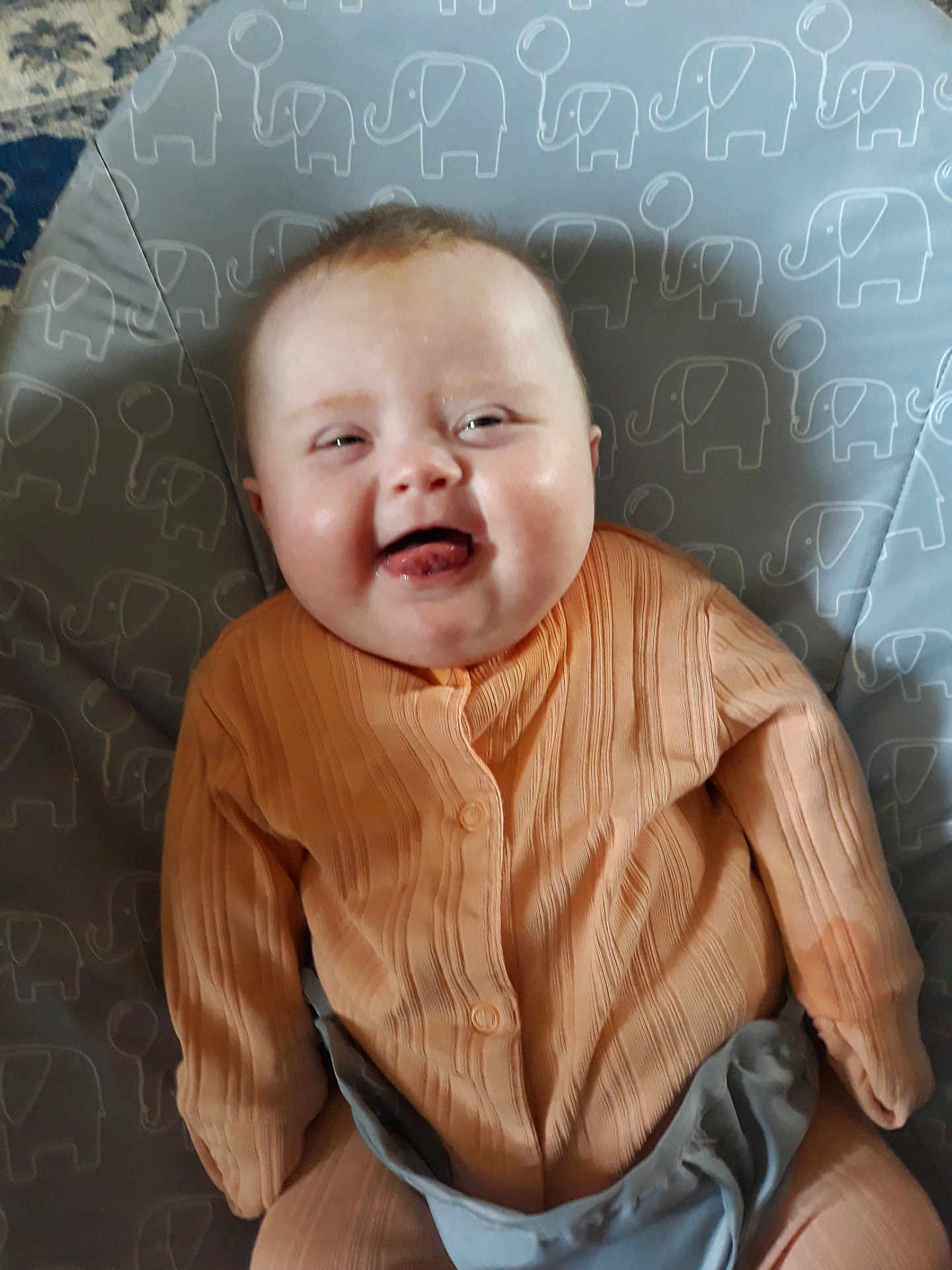 Nevaeh is registered to the contest to win money with this photo: baby, infant, smile, face, clothing, orange_outfit, cushion, elephant_pattern, indoor, child, happy, cute, person, sitting, playful, portrait, head, young_child, fabric, comfort