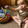 toddler, child, lollipop, candy, basket, carpet, indoor, onesie, cute, curious, sitting, toy, snack, person, baby, floor, wooden_furniture, expression, holding, room