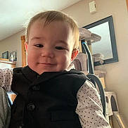 Colton is registered to the contest to win money with this photo: baby, child, vest, shirt, smile, face, indoor, living_room, furniture, mirror, cat_tree, vacuum_cleaner, wooden_frame, person, cute, portrait, young, home, cozy, happy