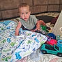 toddler, child, toy, blanket, play_mat, truck, green_toy, couch, indoor, carpet, sitting, curious, clothing, bib, floor, home, person, baby, cute, playtime