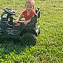 Noah joined the competition — help win amazing prizes! toddler, child, toy_car, grass, outdoor, sunlight, smiling, curly_hair, red_shirt, steering_wheel, greenery, playful, happy, daylight, vehicle, park, nature, kid, summer, fun