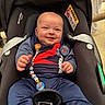 baby, car_seat, infant, smiling, blue_clothing, pacifier_clip, paris_saint_germain, happy, child, seatbelt, indoor, person, cute, casual, sporty, head, face, hands, footwear, comfort