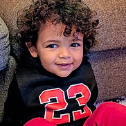 Malik a rejoint le concours — aidez-le/la à gagner de superbes lots ! black_hoodie, casual_clothing, child, couch, cozy, curly_hair, cute, face, happy, indoor, number_23, person, playful, portrait, red_pants, relaxed, sitting, smiling, toddler, young_child