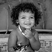 Malik a rejoint le concours — aidez-le/la à gagner de superbes lots ! background, beads, black_and_white, child, curly_hair, cute, depth_of_field, expression, face, hand, happy, motorcycle_toy, necklace, outdoor, playful, portrait, skin, smiling, toddler, toy