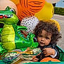 Malik participe au concours pour gagner de l'argent avec cette photo : balloons, child, colorful, curly_hair, cute, dinosaur_balloon, face, festive, green_wagon, happy, orange_balloon, outdoor, person, playful, sidewalk, toddler, toy, wagon, white_balloon, yellow_balloon