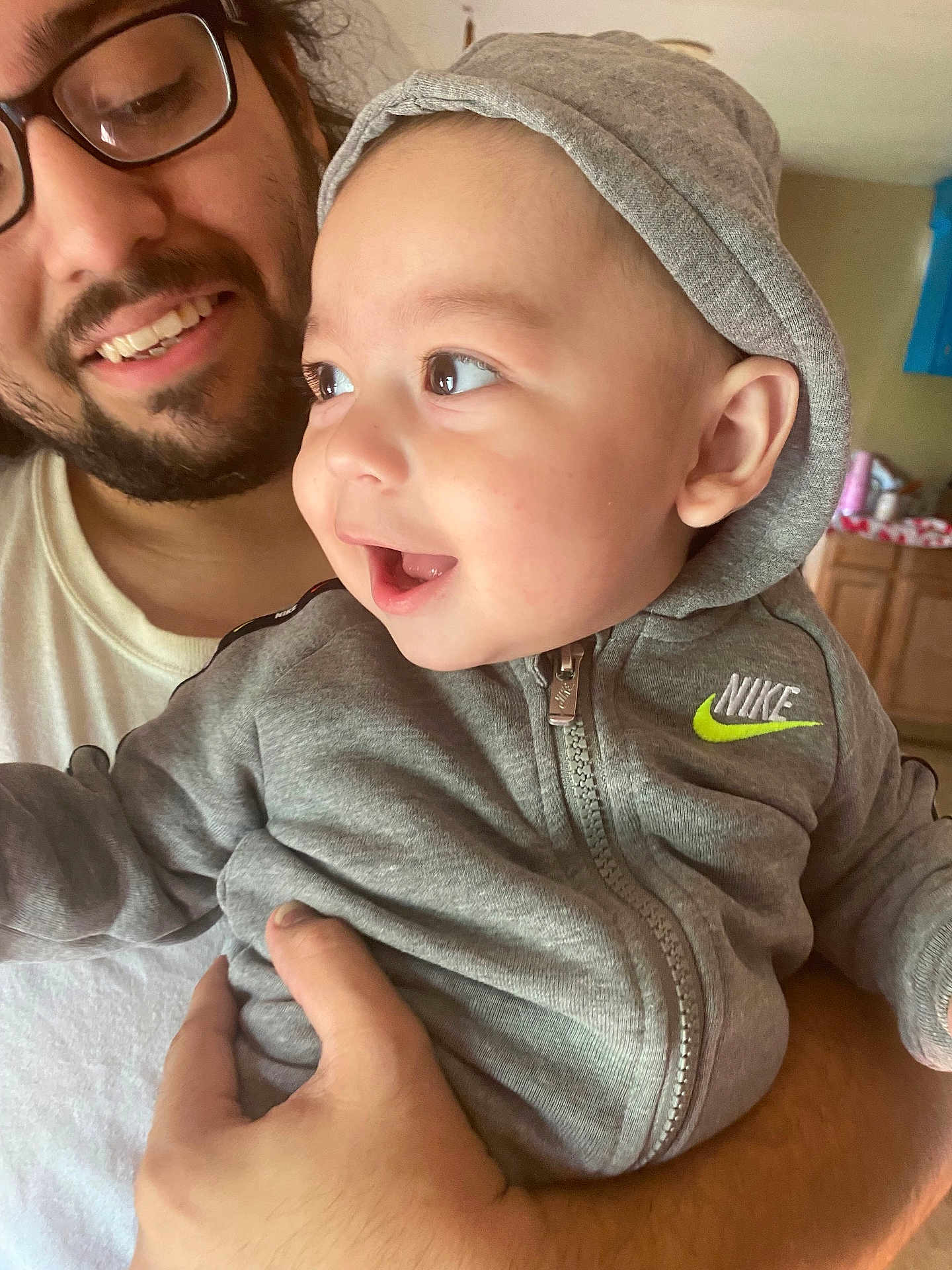 Cruz is registered to the contest to win money with this photo: baby, child, adult, glasses, hoodie, nike, smile, indoor, person, holding, happy, face, hand, clothing, zipper, beard, casual, curly_hair, closeup, family