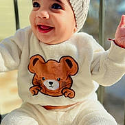 Milo is registered to the contest to win money with this photo: baby, child, smile, hat, knitted_hat, pom_pom, sweater, bear_design, cozy_clothing, warm_clothes, socks, happy, portrait, cute, infant, indoor, natural_light, face, person, apparel